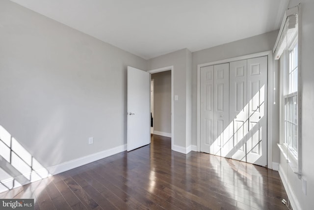 unfurnished bedroom with a closet, baseboards, and dark wood-type flooring