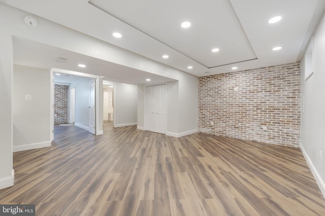 finished below grade area featuring recessed lighting, wood finished floors, baseboards, and brick wall