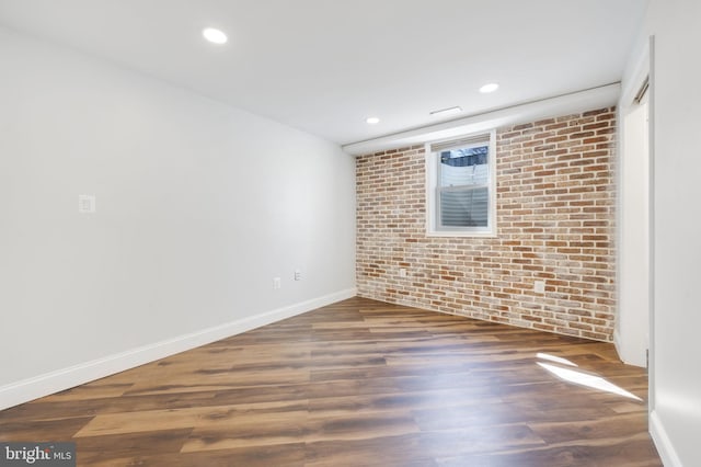 unfurnished room with recessed lighting, brick wall, baseboards, and wood finished floors