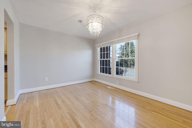 empty room featuring visible vents, baseboards, a notable chandelier, and light wood-style flooring