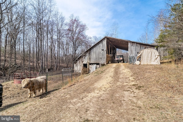 view of side of home featuring fence, an outdoor structure, a pole building, a carport, and driveway