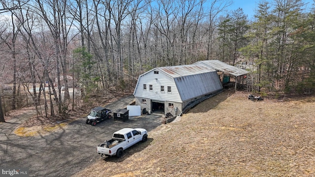 exterior space featuring a forest view, a gambrel roof, and driveway