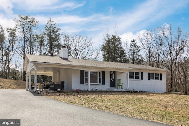 single story home featuring driveway, a chimney, a front lawn, a carport, and brick siding