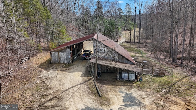 exterior space with a forest view, a carport, an outdoor structure, and dirt driveway