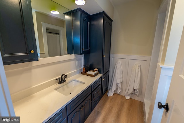 full bathroom with a wainscoted wall, wood finished floors, a shower with shower curtain, a decorative wall, and vanity