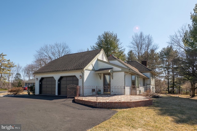 view of front facade featuring driveway, an attached garage, a shingled roof, a chimney, and brick siding