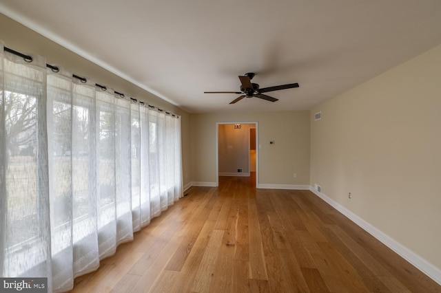 spare room featuring a ceiling fan, baseboards, and light wood finished floors