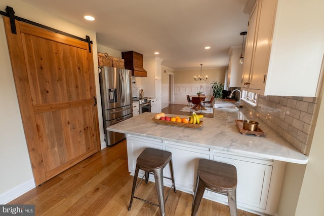 kitchen with a peninsula, a sink, stainless steel appliances, a barn door, and backsplash