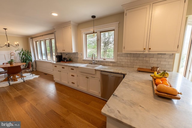 kitchen with light wood-type flooring, a sink, decorative light fixtures, backsplash, and dishwasher