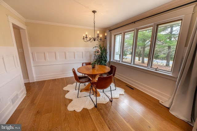 dining room with crown molding, a notable chandelier, wood finished floors, and visible vents