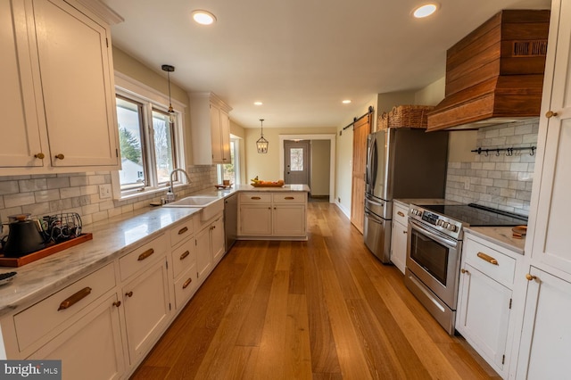 kitchen with a sink, stainless steel appliances, a barn door, a peninsula, and custom exhaust hood