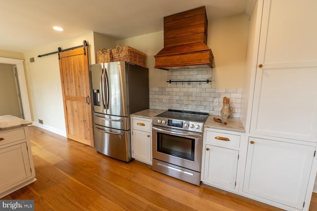 kitchen with light wood finished floors, backsplash, a barn door, appliances with stainless steel finishes, and custom exhaust hood