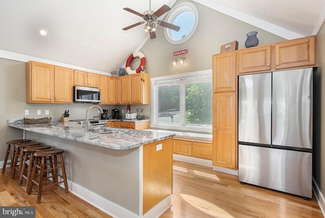 kitchen featuring appliances with stainless steel finishes, light wood-style floors, a sink, and a peninsula