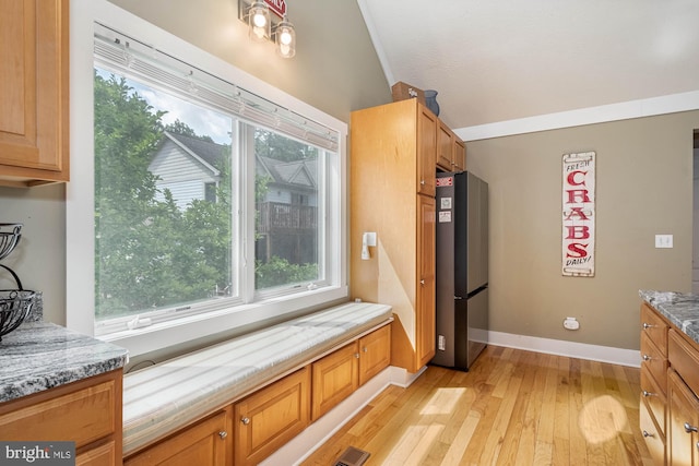 kitchen with light wood-type flooring, baseboards, light stone counters, and freestanding refrigerator