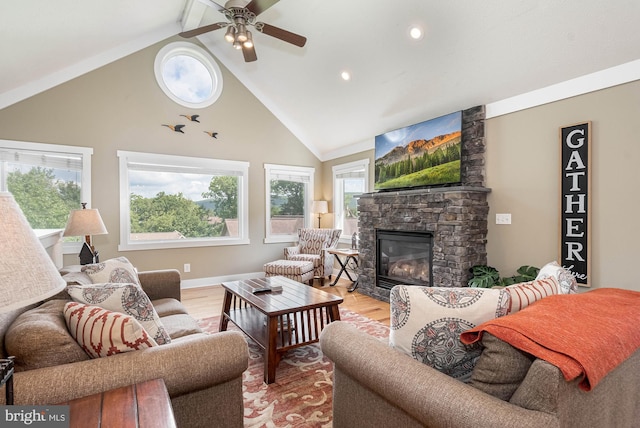 living area with ceiling fan, high vaulted ceiling, a stone fireplace, and light wood-type flooring