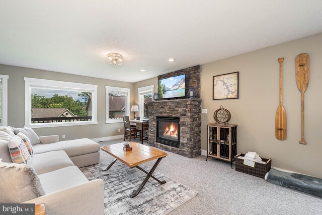 carpeted living area featuring baseboards and a stone fireplace