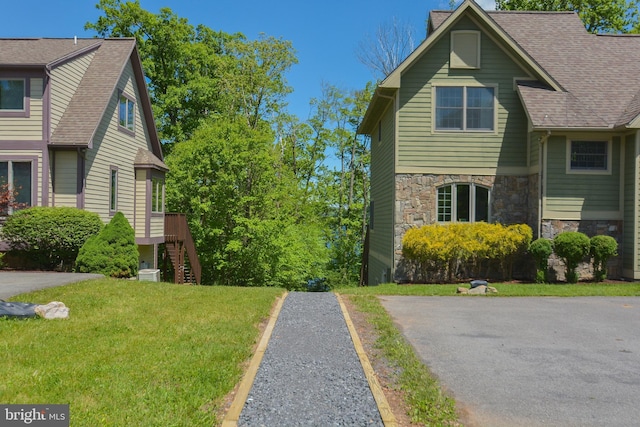 view of side of home featuring central AC, a yard, roof with shingles, and stone siding