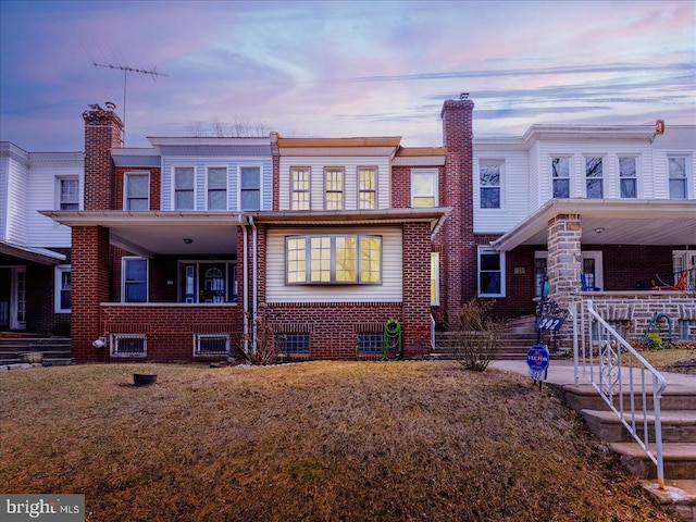 view of front of house with brick siding, covered porch, a chimney, and a lawn