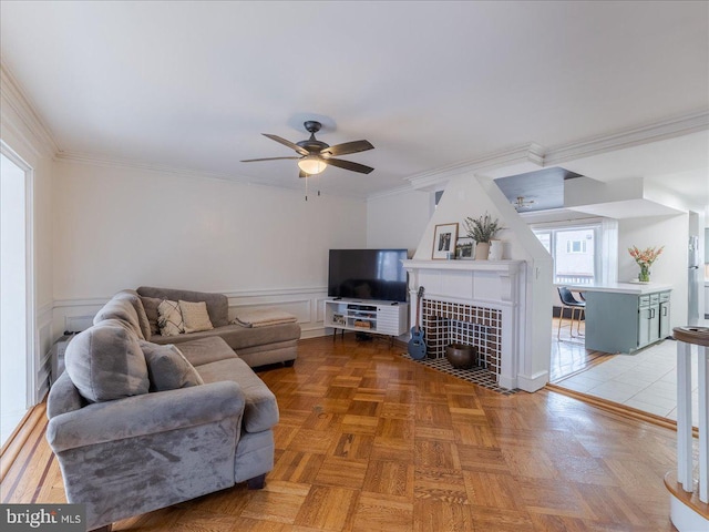 living area featuring ceiling fan, crown molding, a decorative wall, and wainscoting