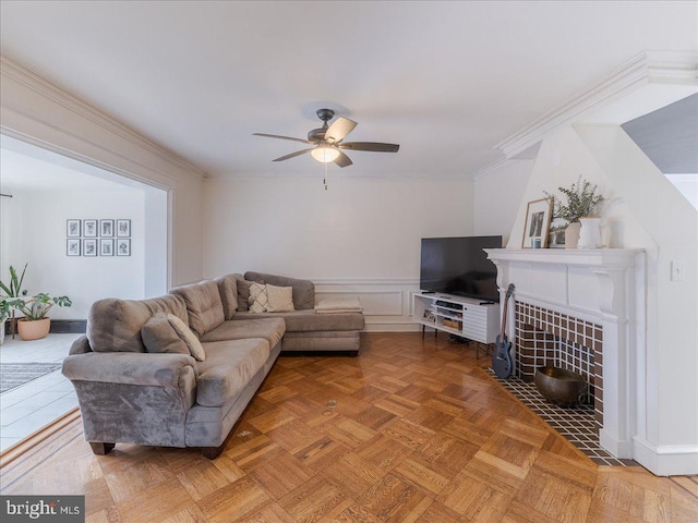 living area featuring a decorative wall, a wainscoted wall, a ceiling fan, and ornamental molding