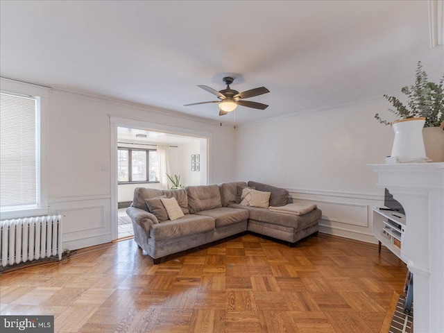 living room with a wainscoted wall, radiator, crown molding, and ceiling fan