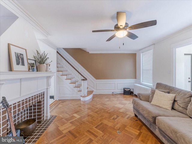 living area featuring radiator heating unit, stairway, a fireplace, a decorative wall, and crown molding