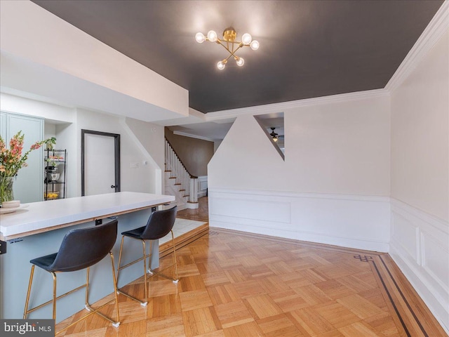 interior space featuring crown molding, a breakfast bar area, light countertops, wainscoting, and a notable chandelier