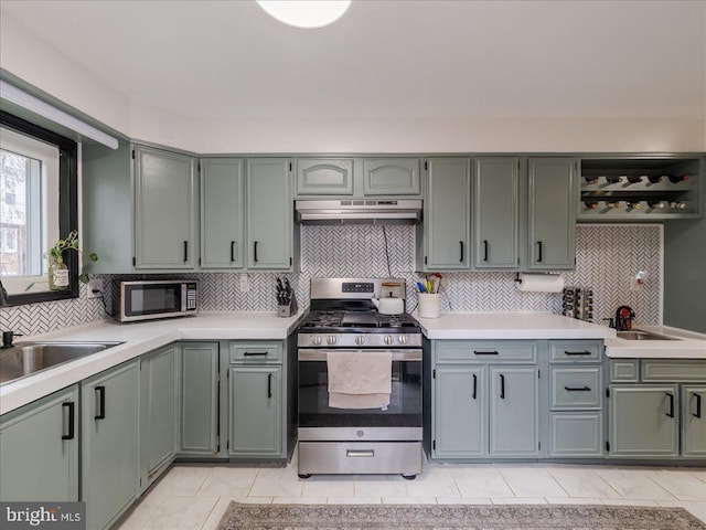 kitchen with under cabinet range hood, light countertops, appliances with stainless steel finishes, and a sink