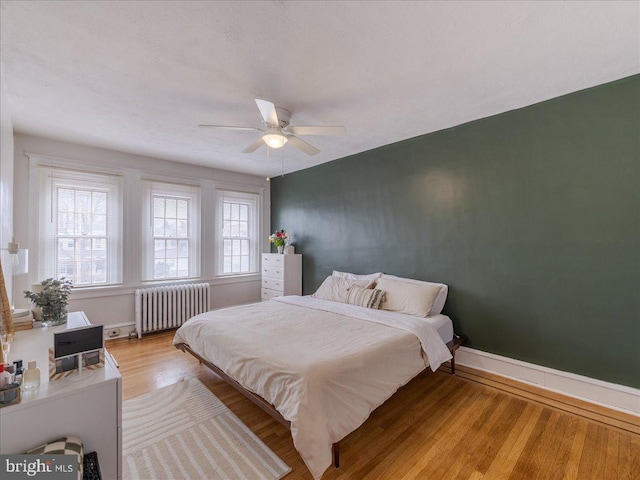 bedroom with baseboards, a ceiling fan, light wood-style flooring, and radiator heating unit