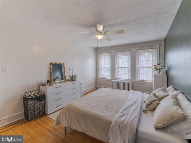 bedroom featuring radiator heating unit, baseboards, light wood-type flooring, and a textured ceiling