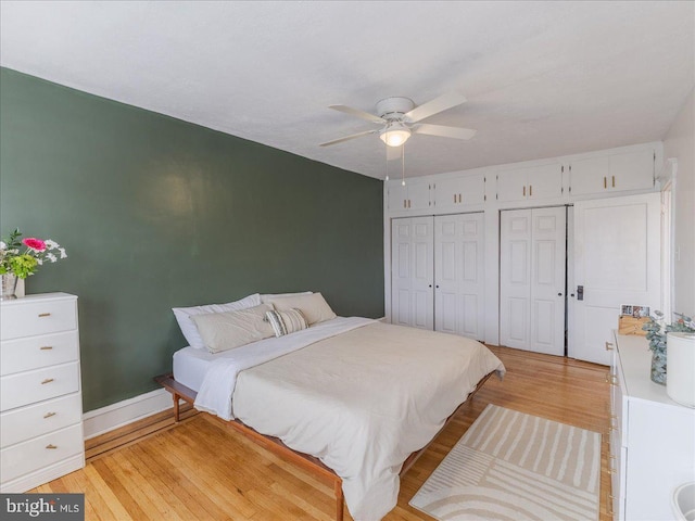 bedroom with light wood-style flooring, two closets, and ceiling fan