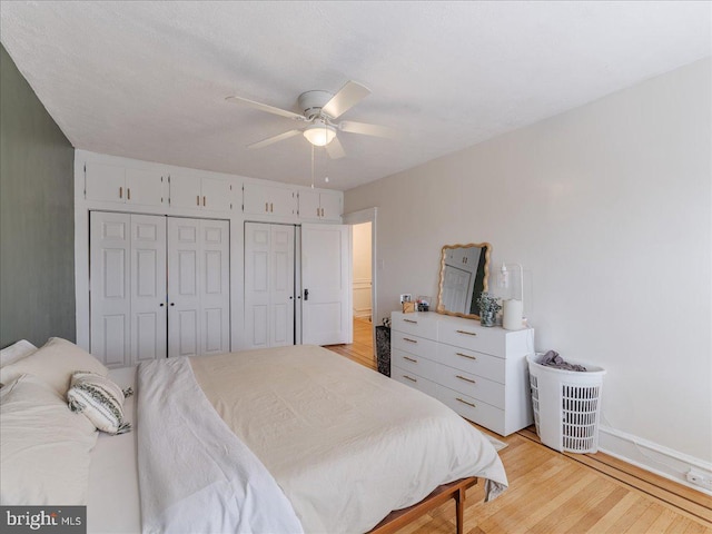 bedroom featuring light wood finished floors, a ceiling fan, and multiple closets