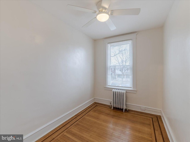 unfurnished room featuring radiator, wood finished floors, baseboards, and ceiling fan