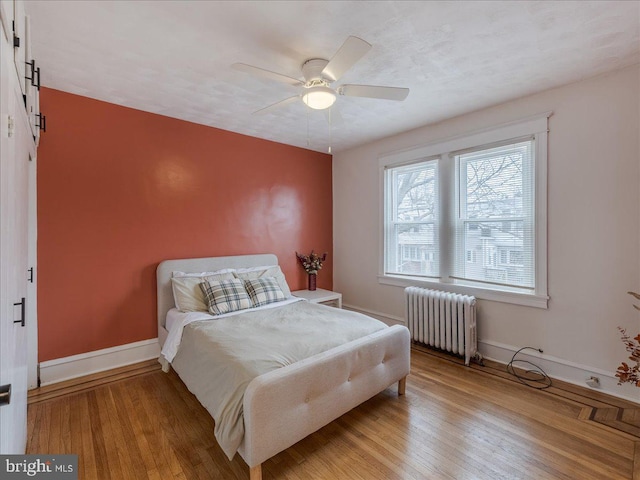 bedroom featuring baseboards, light wood-type flooring, radiator heating unit, and a barn door