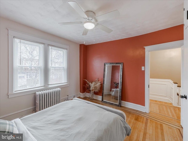 bedroom featuring radiator, wood finished floors, baseboards, and ceiling fan