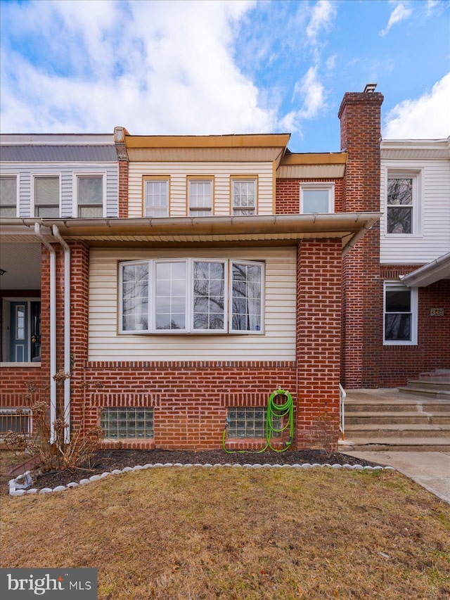 multi unit property featuring brick siding, a chimney, and a front yard