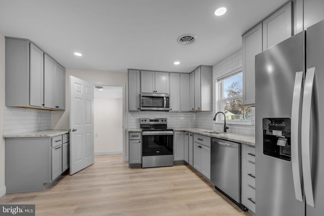 kitchen with light wood finished floors, gray cabinetry, light stone counters, stainless steel appliances, and a sink