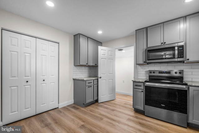 kitchen featuring gray cabinetry, light wood-type flooring, light stone counters, decorative backsplash, and stainless steel appliances