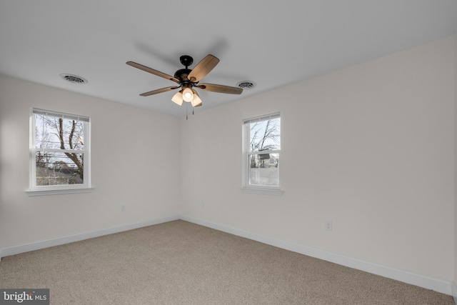 carpeted spare room with a healthy amount of sunlight, visible vents, and baseboards