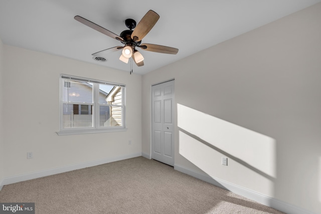 unfurnished bedroom with visible vents, a closet, baseboards, light colored carpet, and ceiling fan