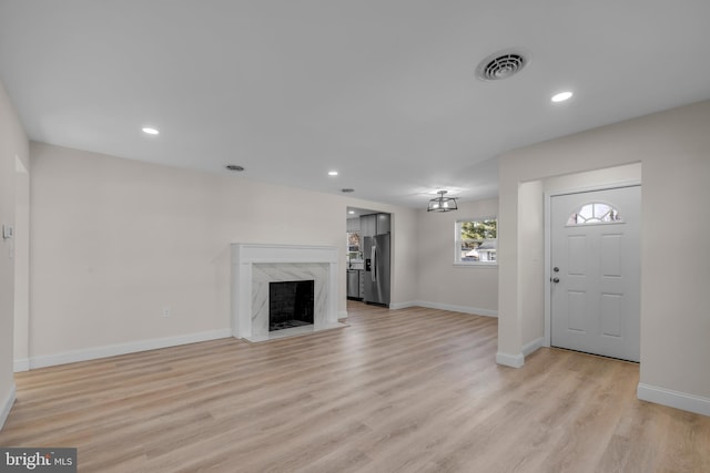 unfurnished living room featuring light wood-style flooring, a fireplace, visible vents, and baseboards