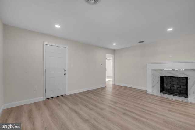 unfurnished living room with a high end fireplace, recessed lighting, light wood-type flooring, and baseboards