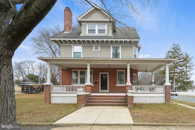 traditional style home with brick siding, covered porch, a chimney, and a front lawn