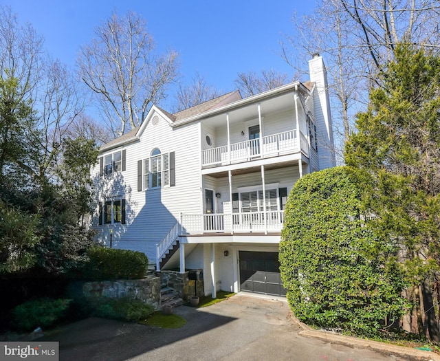 view of front of home featuring stairs, a chimney, driveway, a balcony, and an attached garage