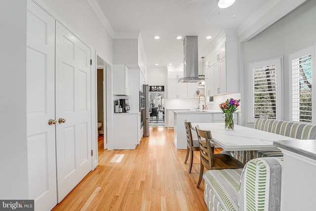 kitchen featuring white cabinets, ornamental molding, island range hood, and light countertops