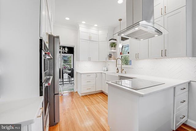 kitchen featuring light wood finished floors, a peninsula, island exhaust hood, white cabinets, and black electric stovetop