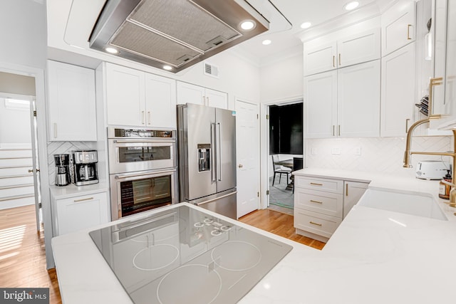 kitchen featuring visible vents, a sink, stainless steel appliances, light wood-style floors, and wall chimney range hood