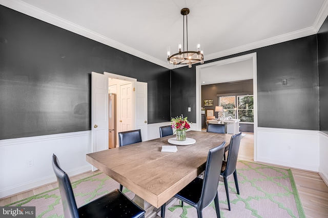 dining room with a notable chandelier, a wainscoted wall, light wood-style flooring, and crown molding