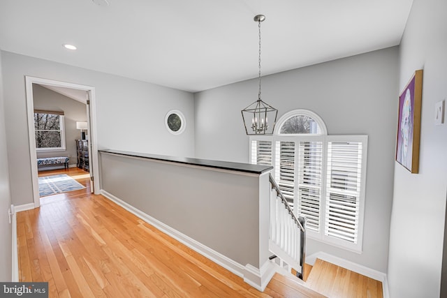 hall with an inviting chandelier, light wood-style flooring, an upstairs landing, and a wealth of natural light