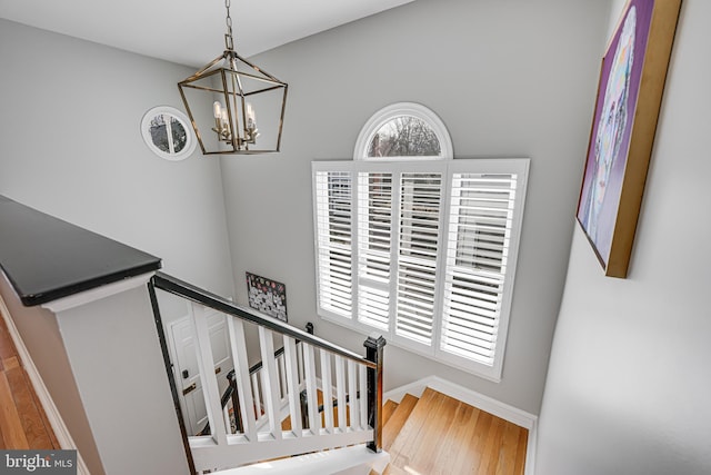 staircase featuring baseboards, a notable chandelier, and wood finished floors